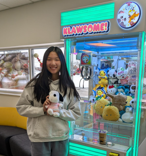 Happy guest holding a Snoopy plush next to a glowing Klawsome claw machine