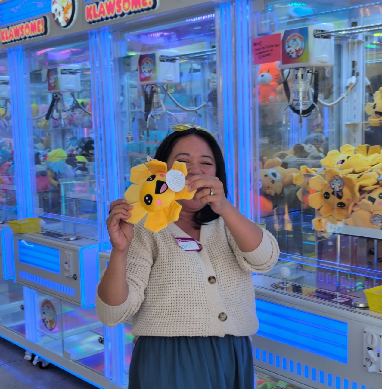 Klawsome team member holding a yellow sunflower plushie in front of claw machines